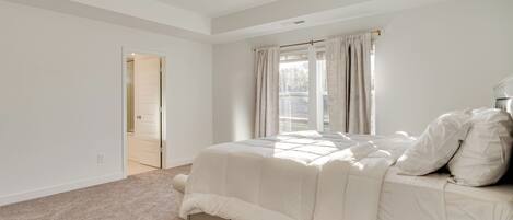 A bedroom with a bed, a window with curtains, and a door leading to another room.