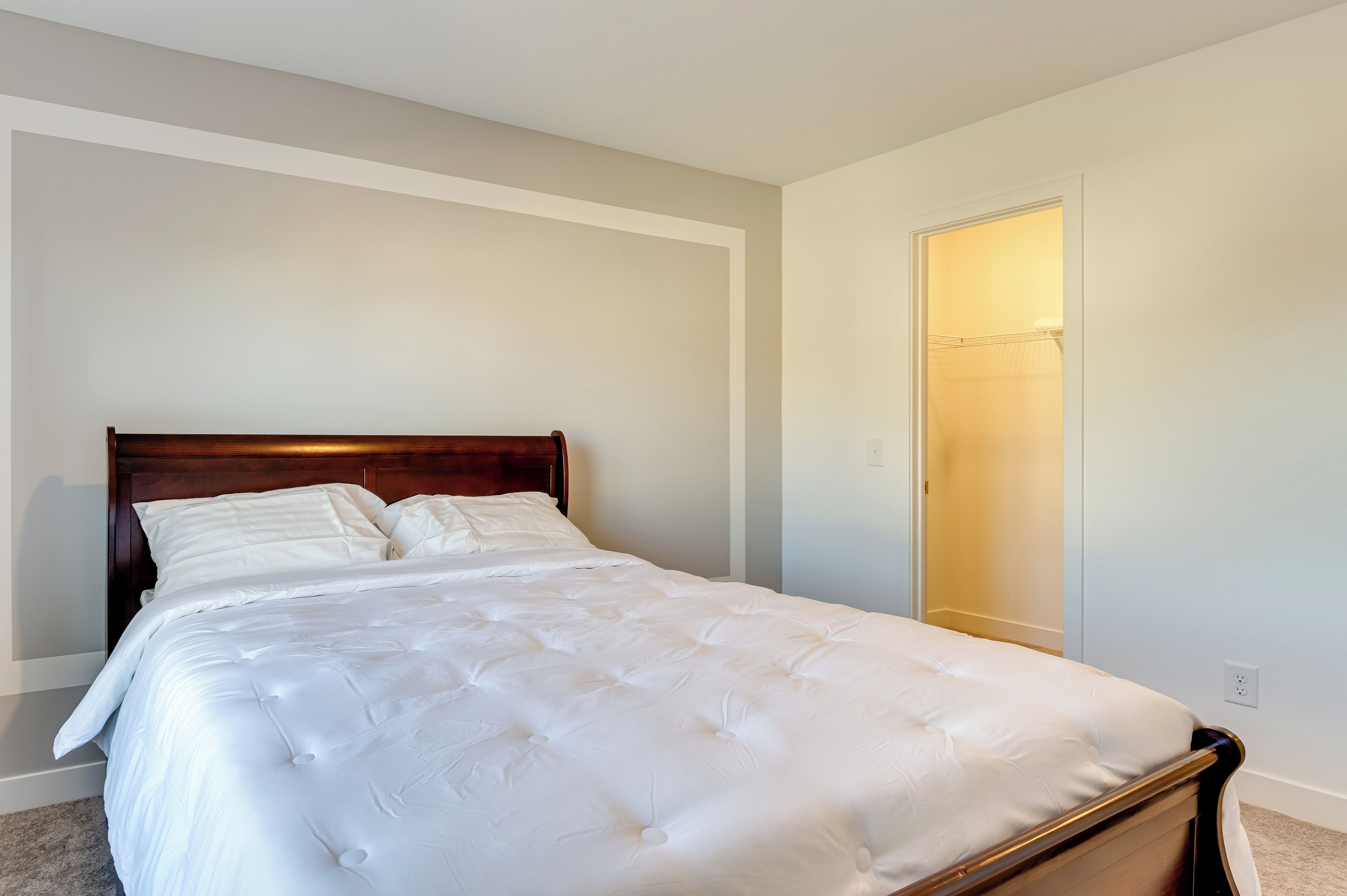 A neatly made bed with a wooden headboard in a room with light-colored walls and a door leading to a closet.