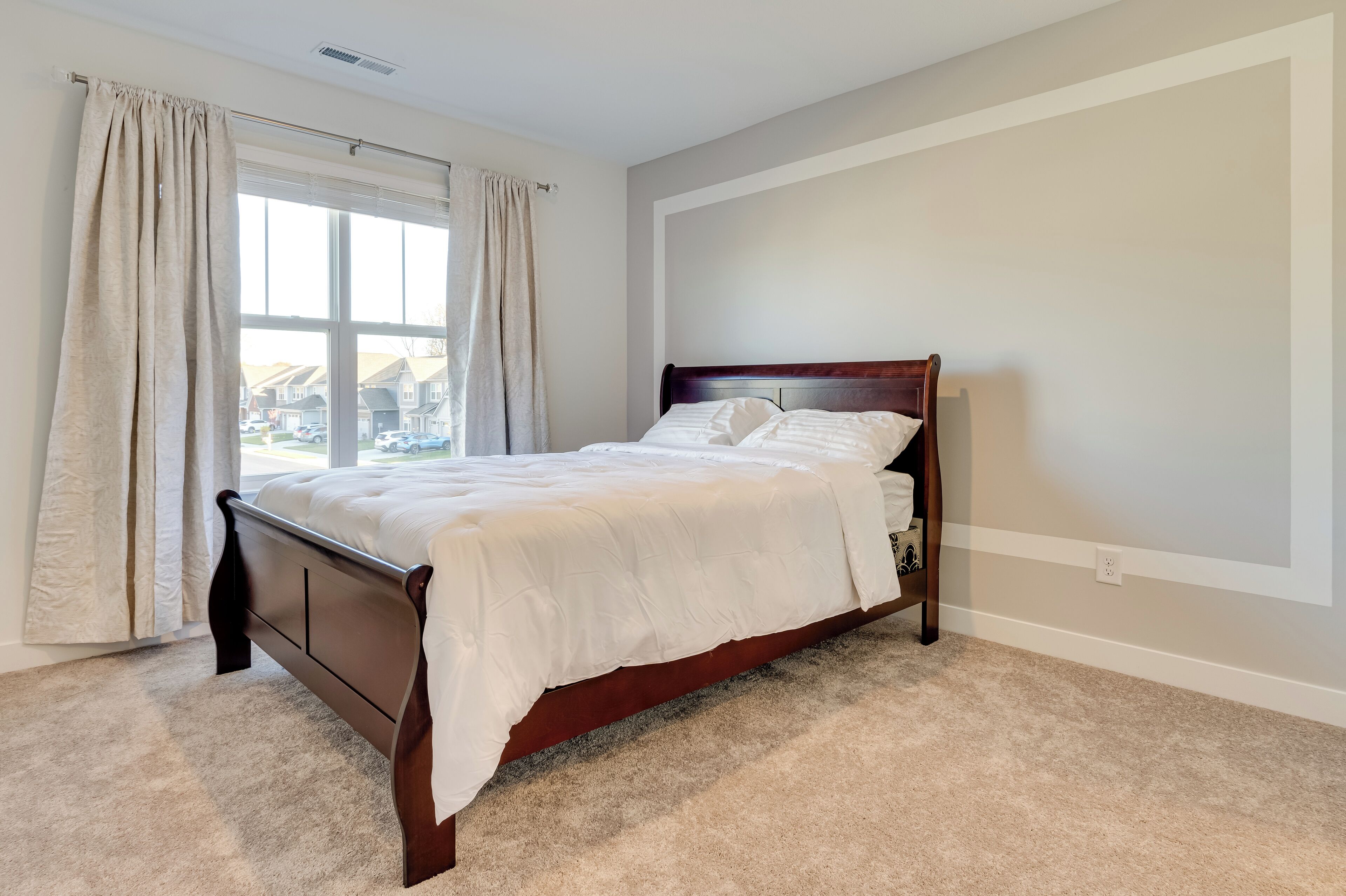 A bedroom with a wooden bed, beige carpet, and a window with curtains.