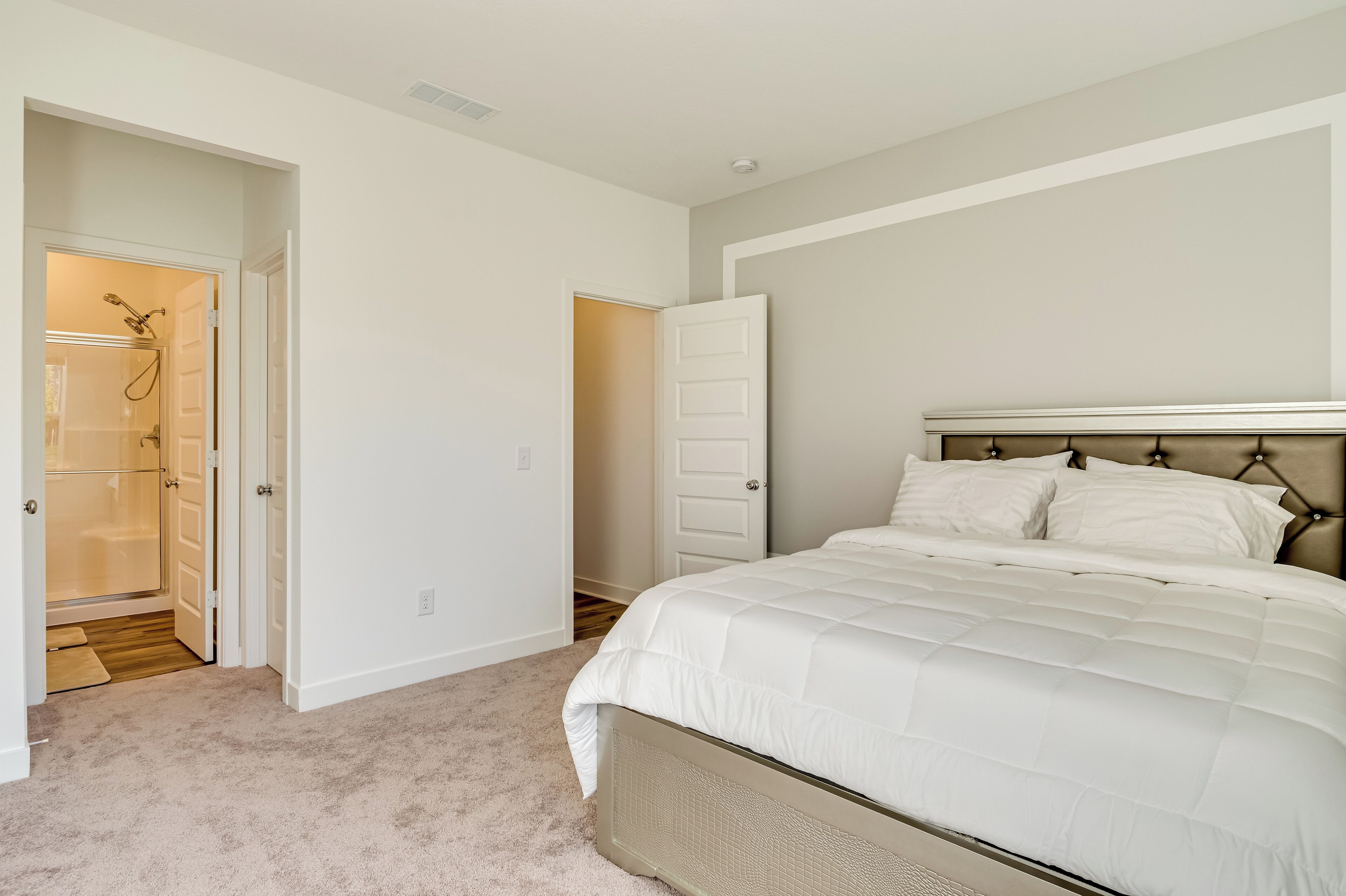 Une chambre avec un grand lit, un dressing et une salle de bain avec douche.