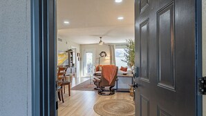 A modern interior with a dining area, a seating area with a chair, and a large dark door. - Fully Appointed Upper Floor Condo with Mountain-Canyon-Pool-Golf Course Views (Tucson)