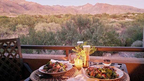 A dining table with plates of food and drinks, set against a mountainous backdrop. - Fully Appointed Upper Floor Condo with Mountain-Canyon-Pool-Golf Course Views (Tucson)