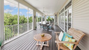En overdækket veranda med træterrasse, hvide gelændere og et bord med stole.