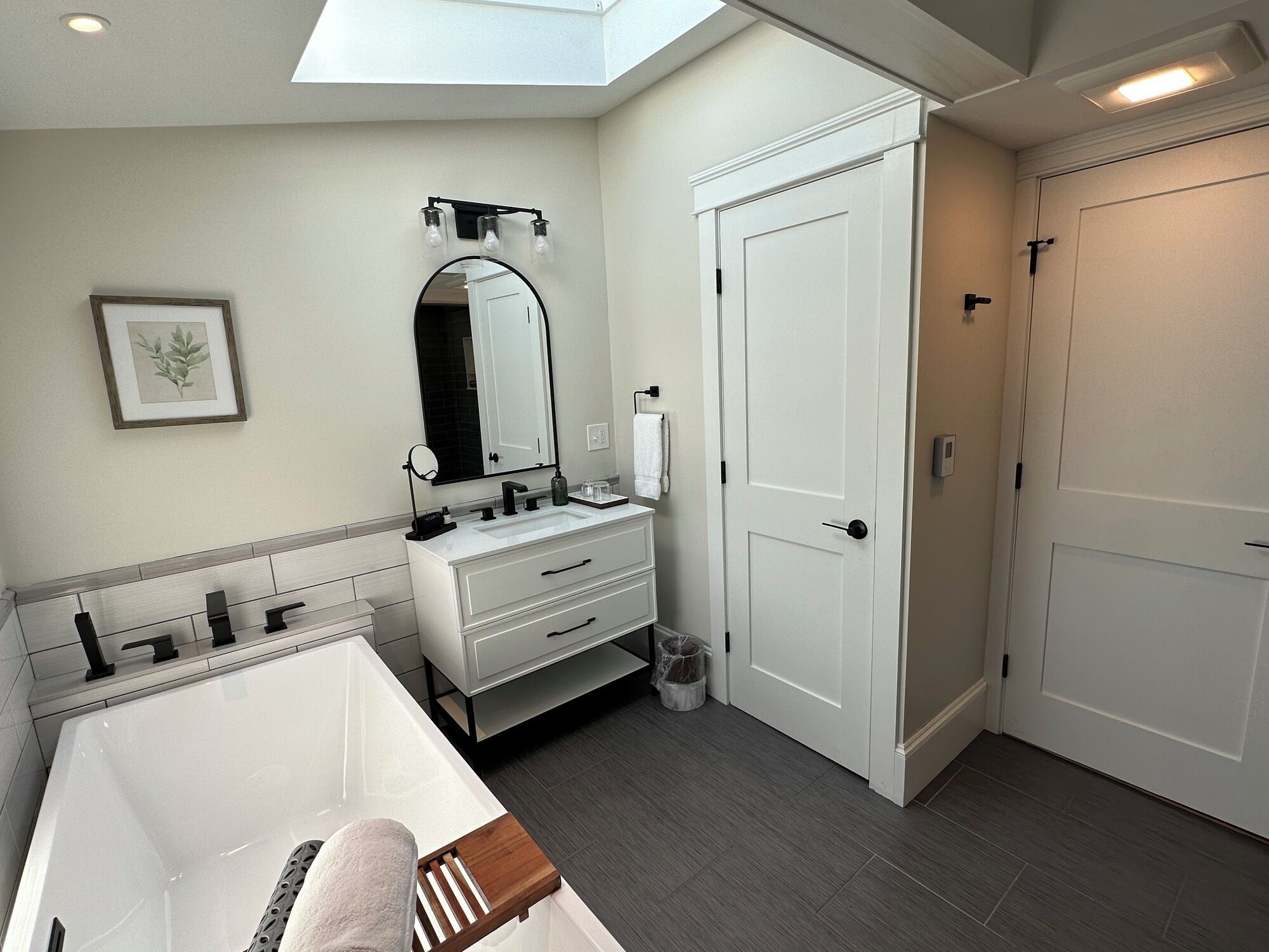 Une salle de bain moderne dotée d’un puits de lumière, d’un grand miroir, d’une baignoire et d’un meuble-lavabo blanc.