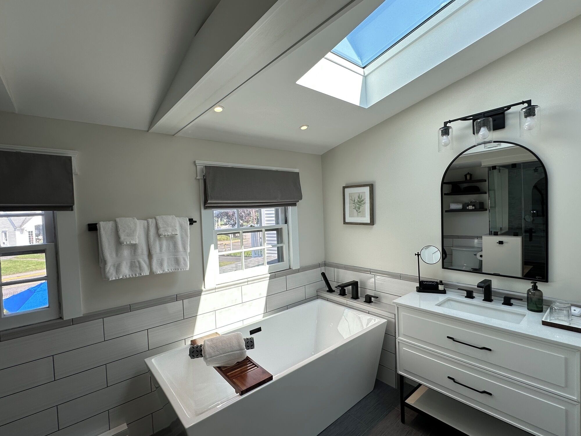 Un baño moderno con tragaluz, bañera, tocador con espejo y ventana con vistas al exterior.