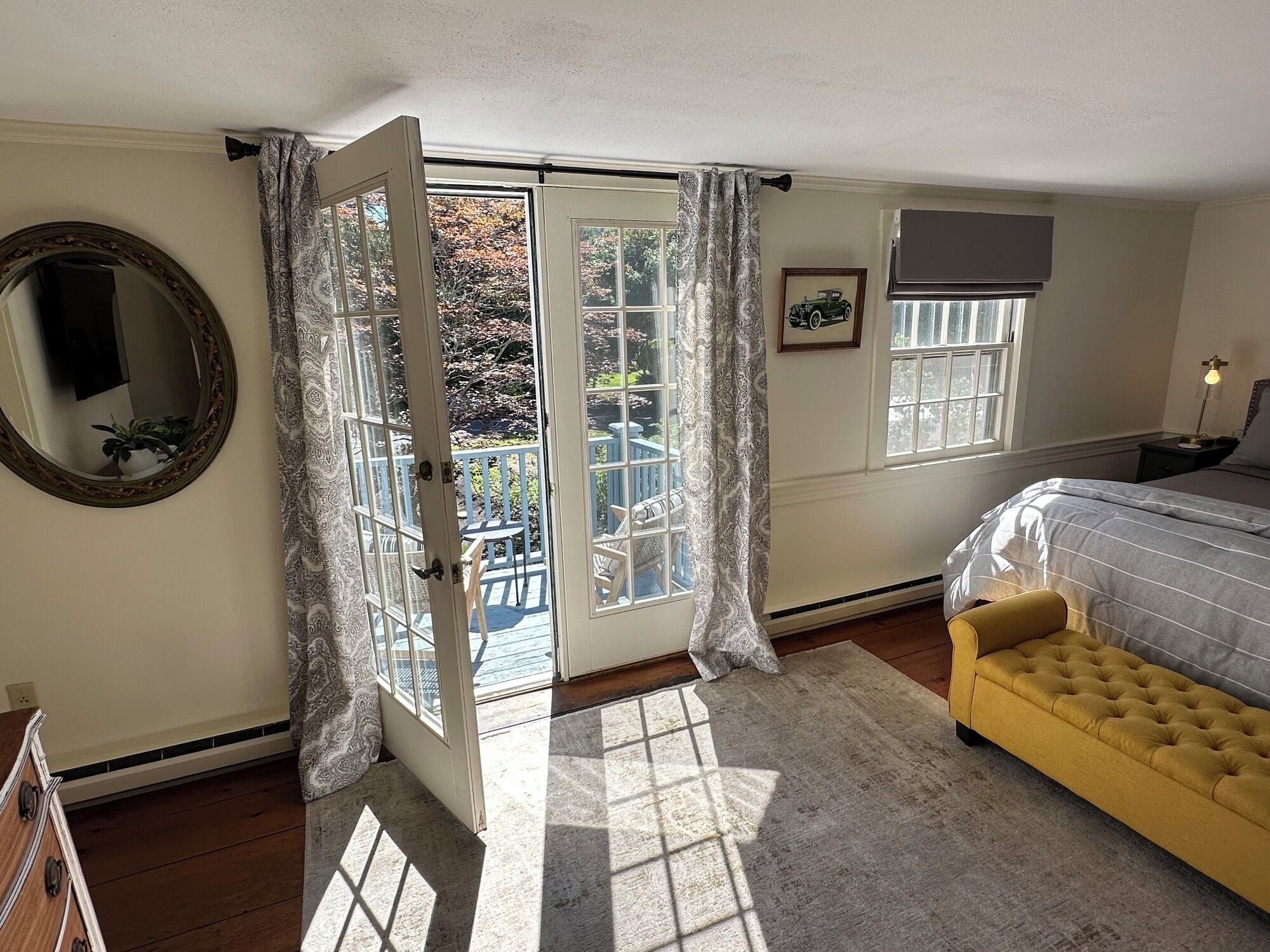 Un dormitorio con cama, un sillón amarillo, un espejo grande y vistas a un balcón con una silla.