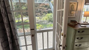 A room with a large sliding glass door leading to a garden, a vintage-style dresser, and a framed artwork on the wall. - Inn at Perkins Cove (Ogunquit)