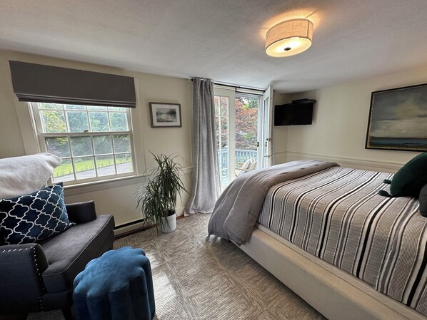 A bedroom with a bed, a chair, a potted plant, a window, and a painting on the wall. - Inn at Perkins Cove (Ogunquit)