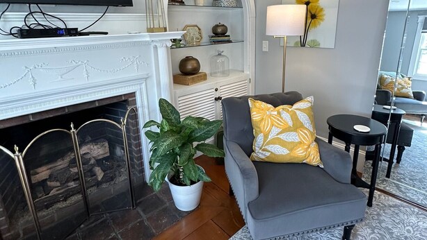 A living room with a fireplace, a sofa, a side table, a lamp, and a television mounted on the wall. - Inn at Perkins Cove (Ogunquit)