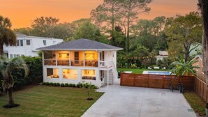 A two-story house with a covered porch, a swimming pool, and a well-maintained lawn. - Updated 4th row beach home, private pool, fenced in yard, and putting green! (Hilton Head)
