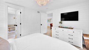 A bedroom with a large bed, white dresser, and a TV mounted on the wall. - Updated 4th row beach home, private pool, fenced in yard, and putting green! (Hilton Head)