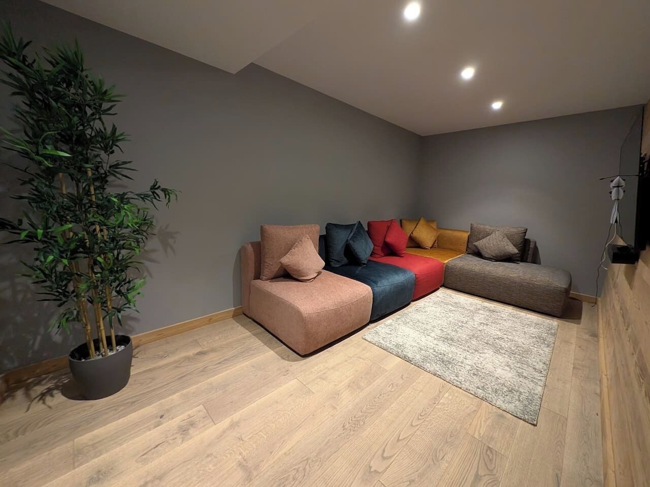 A modern living room with a sofa set, a potted plant, and a wooden floor.