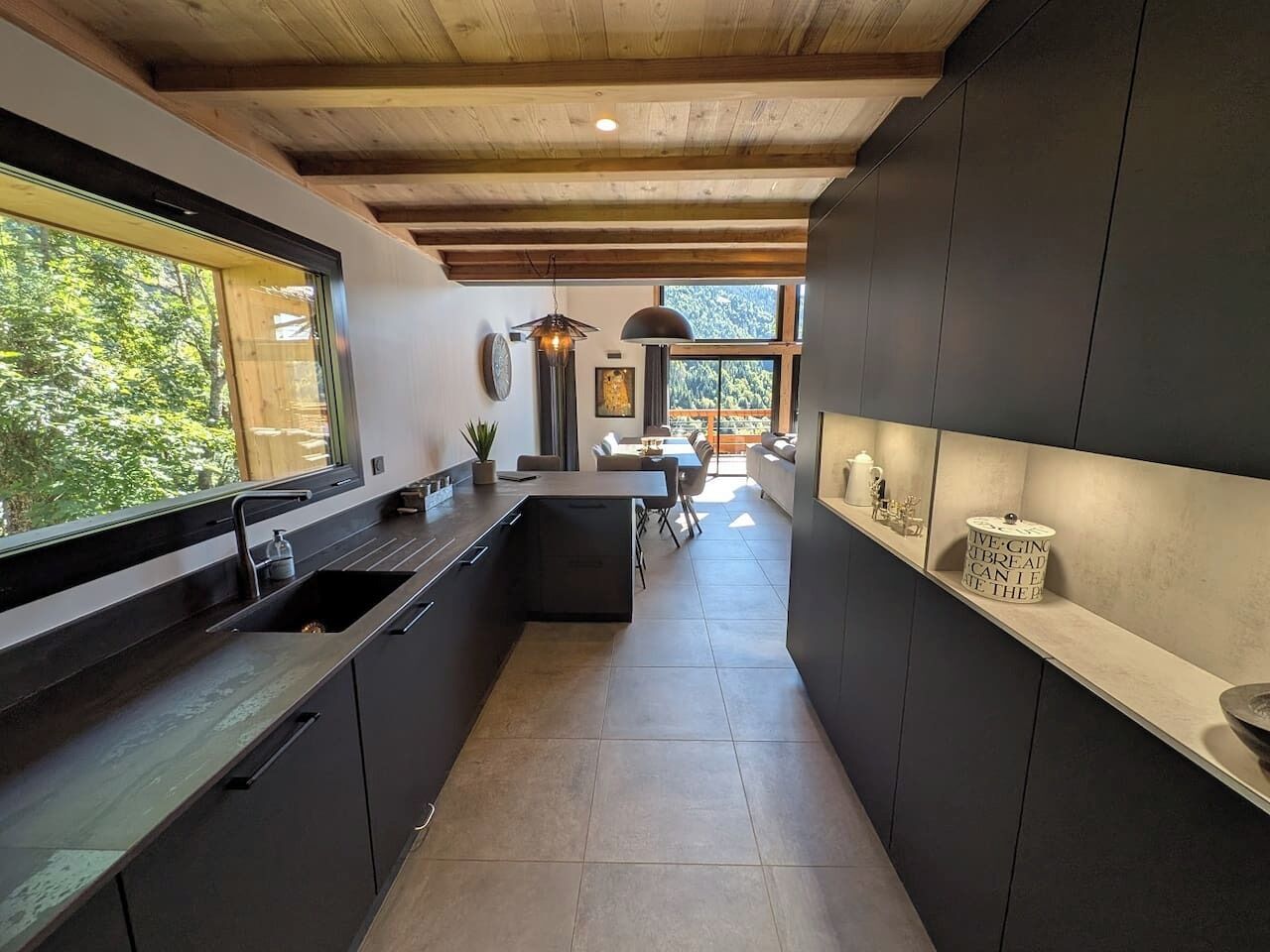Une cuisine moderne avec des meubles de couleur sombre, un îlot central et une vue sur l’espace repas.