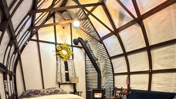 Un interior acogedor con cama, sofá y mesa, destacando una estructura de techo curva y una chimenea.
