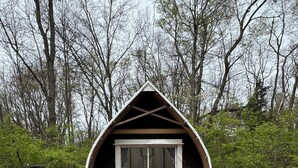 Una pequeña cabaña de madera con techo inclinado, una puerta corrediza de vidrio y dos sillas afuera.