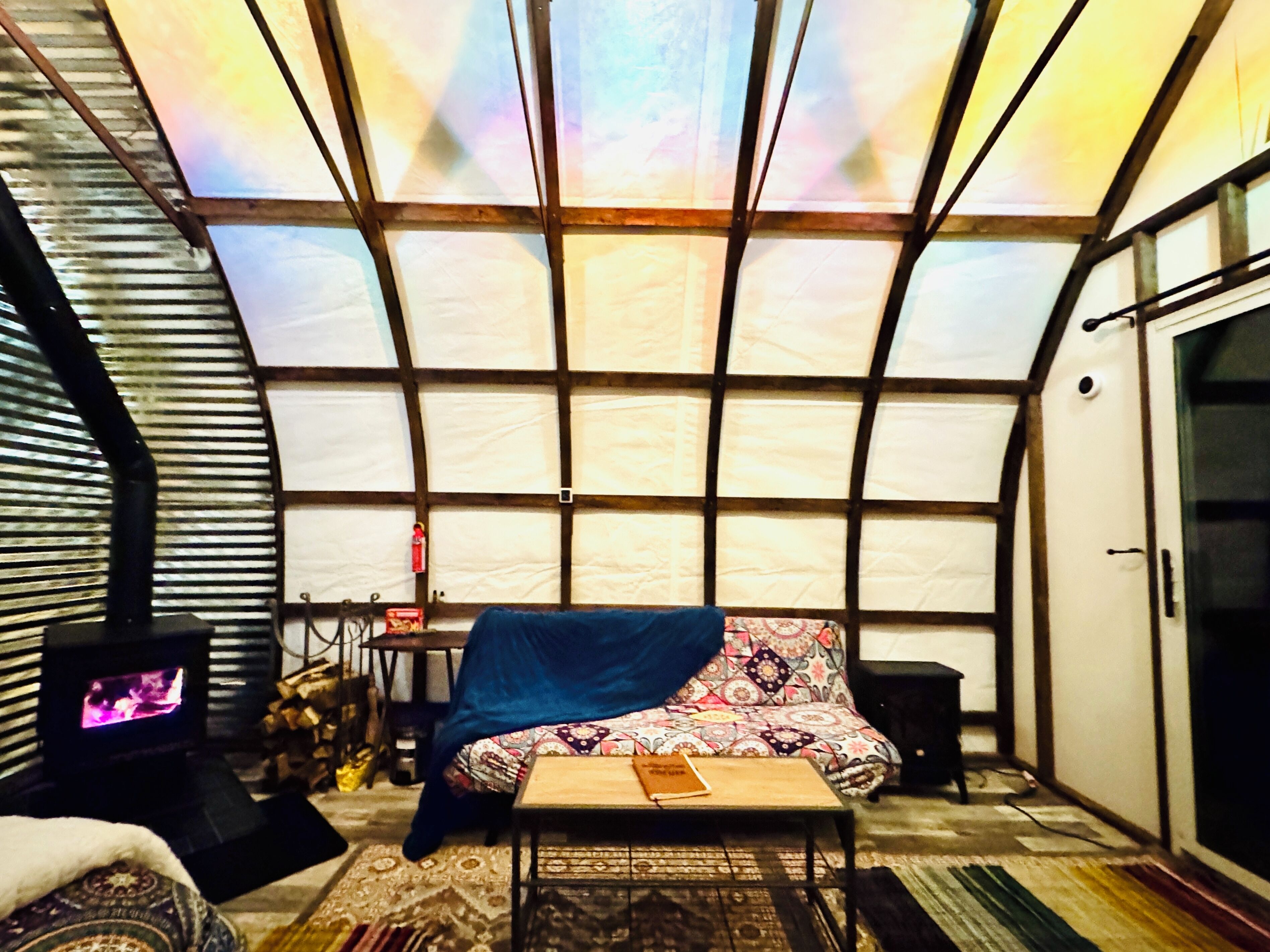 A cozy interior with a large window, a bed, a table, and a fireplace.