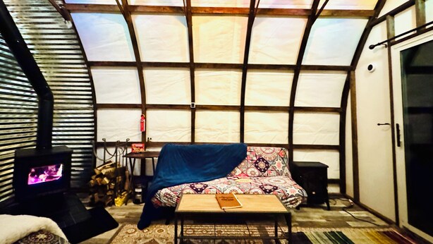 A cozy interior with a large window, a bed, a table, and a fireplace.