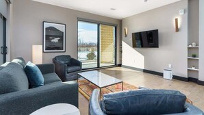 A modern living room with a sofa, armchair, and coffee table, a TV mounted on the wall, and a large window with a view of the outdoors. - Stylish Getaway w/ Balcony & Scenic Mountain Views (Denver)