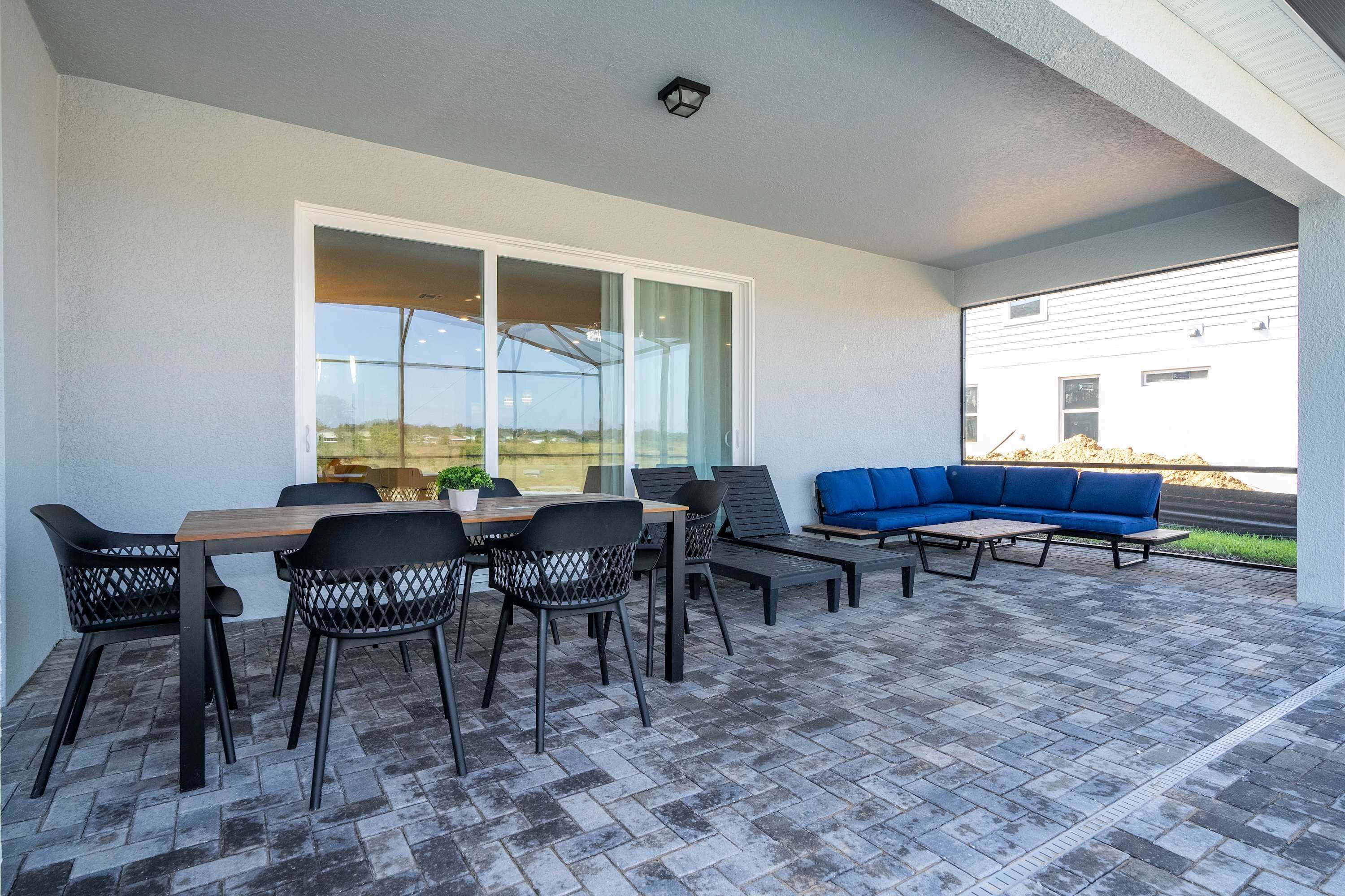 Une terrasse extérieure avec une table et des chaises en bois, un canapé bleu et une vue sur un immeuble à travers de grandes fenêtres.
