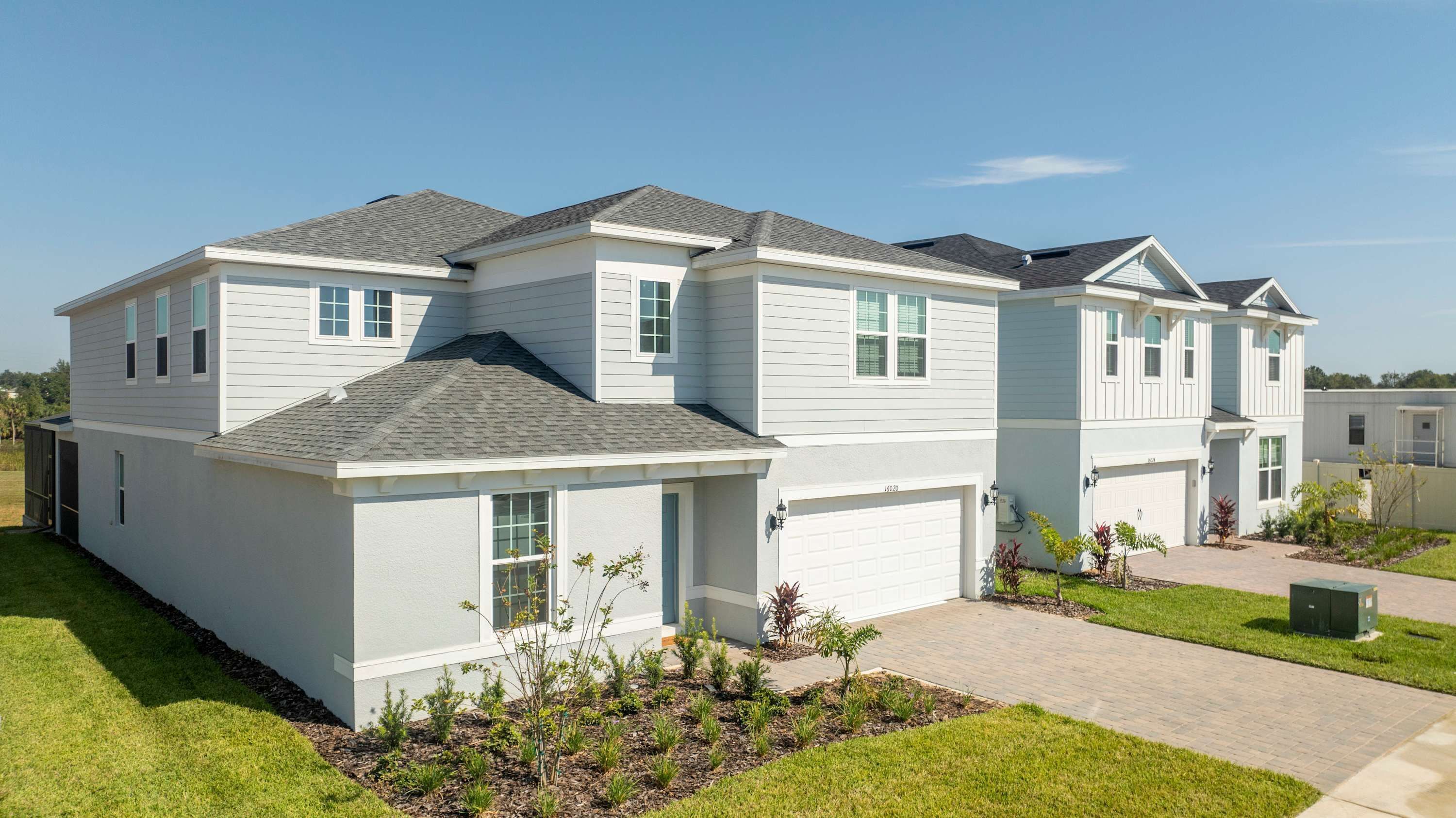 A two-story residential building with a garage, a small front yard with landscaping, and a clear sky.
