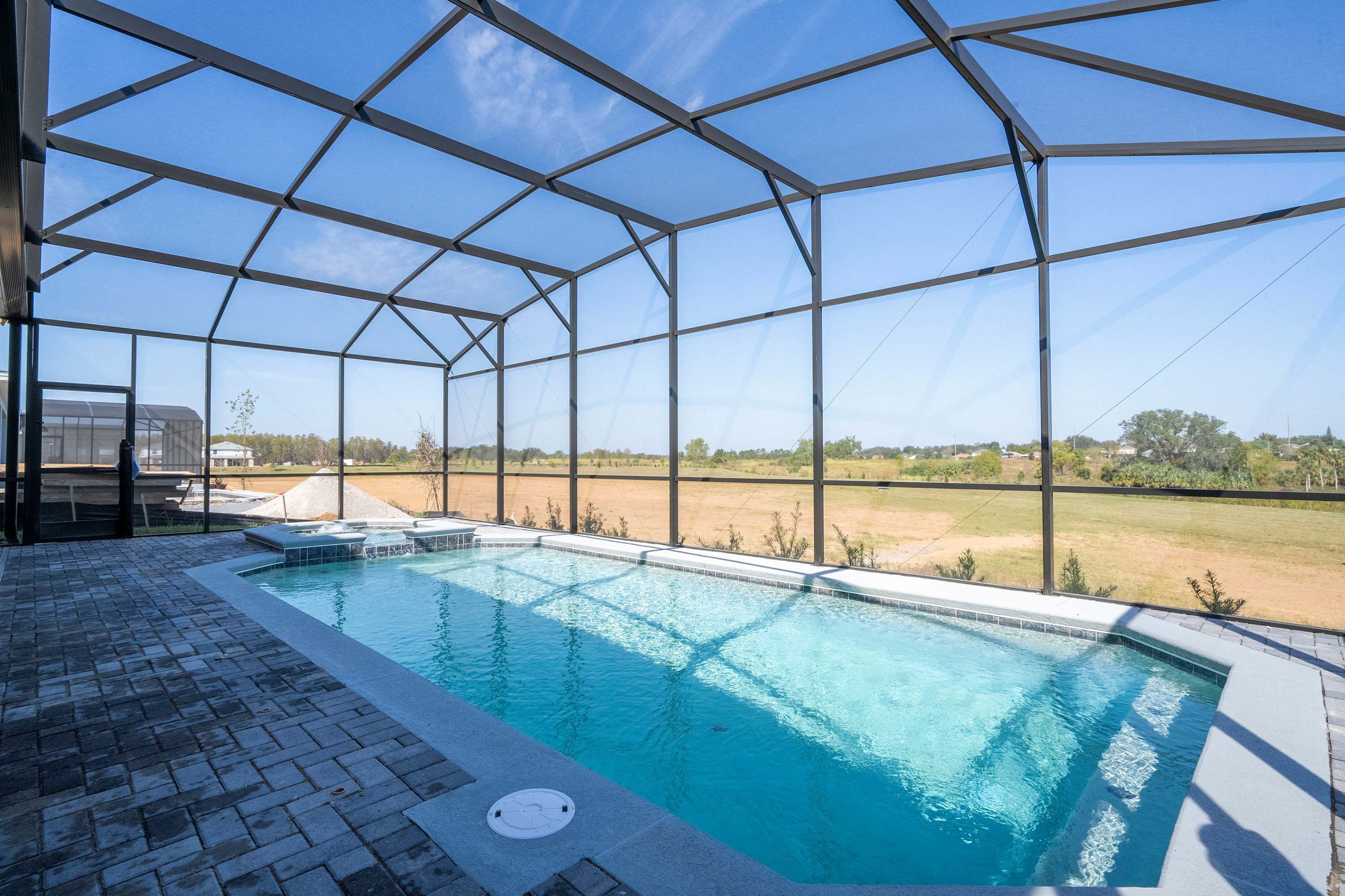 An indoor swimming pool with a clear view of the surrounding landscape through a large, open-sided structure.