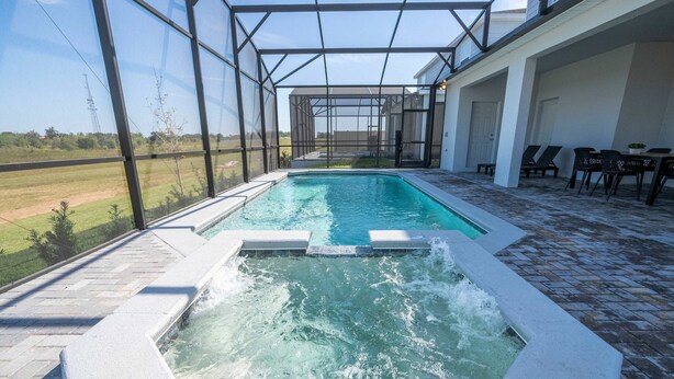 Une piscine agrémentée d’une cascade, entourée d’une terrasse couverte avec des chaises et des tables.