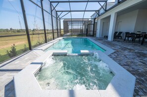 A swimming pool with a waterfall feature, surrounded by a covered patio with chairs and tables. - 16020 Spacious Family Home 8BD Perfect For Your Vacation (Clermont)