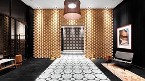 En moderne hotellobby med et mønstret gulv, en central søjle og en stor lysekrone.