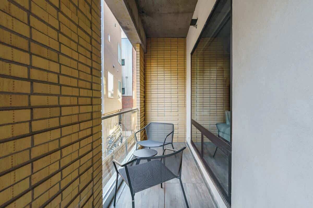 Un balcon étroit avec un mur en briques, une porte vitrée et deux chaises.
