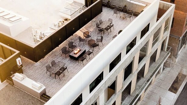 En udendørs terrasse med flere siddeområder, et bålsted og udsigt til bygningens indre.