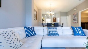A modern living room with a white sectional sofa, patterned throw pillows, and a dining area in the background.