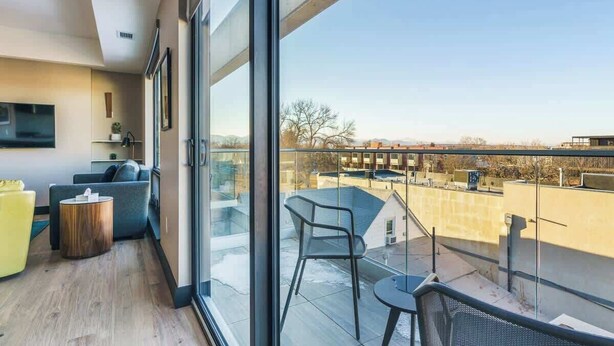 Un appartement moderne doté d’un balcon, d’un canapé, d’une petite table et d’un téléviseur fixé au mur.