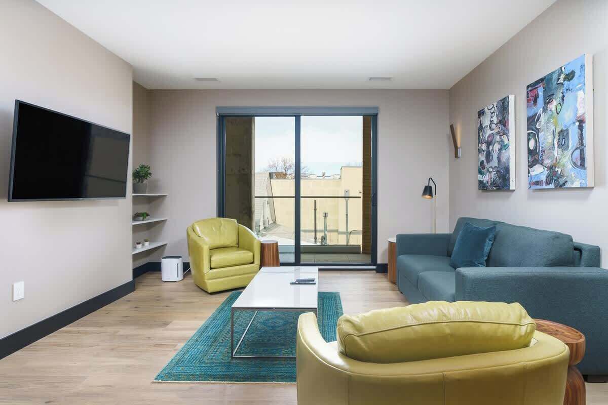 A modern living room with a flat-screen TV, a sofa, a yellow armchair, and a coffee table.
