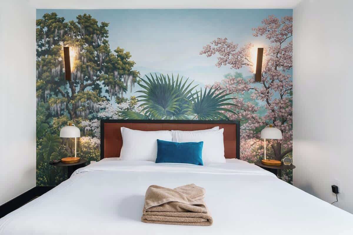 Une chambre d’hôtel avec un grand lit, une tête de lit, deux lampes de chevet et une fresque murale.