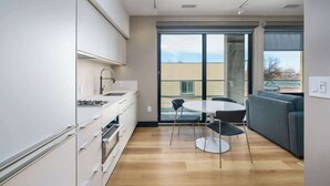 A modern kitchen with white cabinets, a round dining table with four chairs, and a large sliding glass door leading to a balcony. - Designer Studio w/ Balcony & Rooftop Patio on Tennyson Street (Denver)