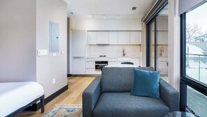 A modern apartment with a grey sofa, a small bed, and a kitchen in the background. - Designer Studio w/ Balcony & Rooftop Patio on Tennyson Street (Denver)