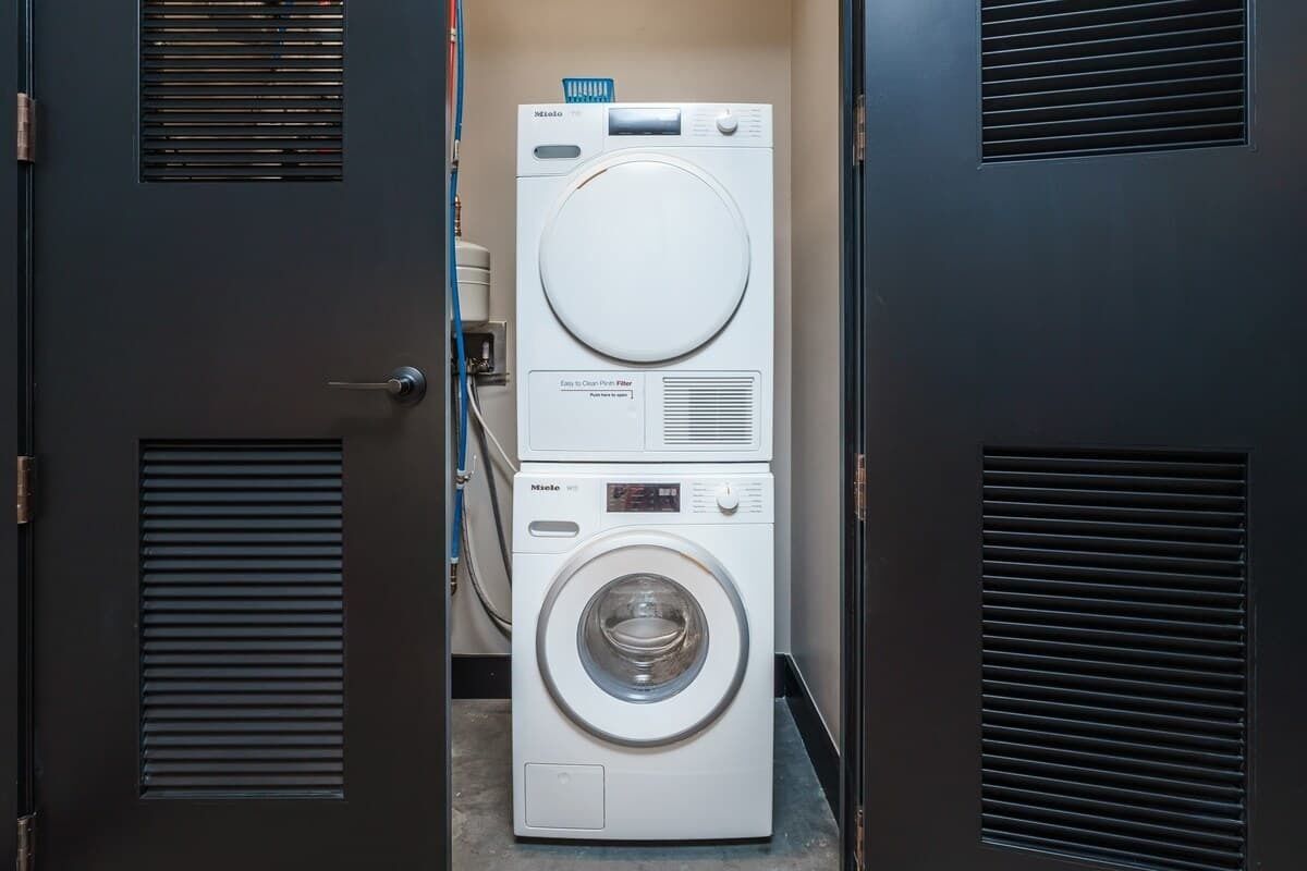 A compact, modern laundry room with a front-loading washer and dryer, a control panel, and a small window.