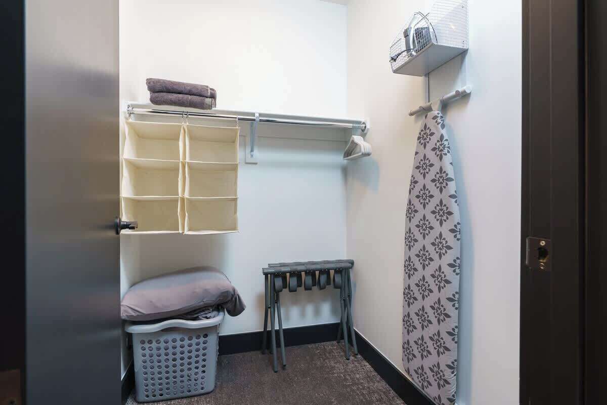 A compact bathroom with a towel rack, a hanging shower curtain, a laundry basket, and a small table.