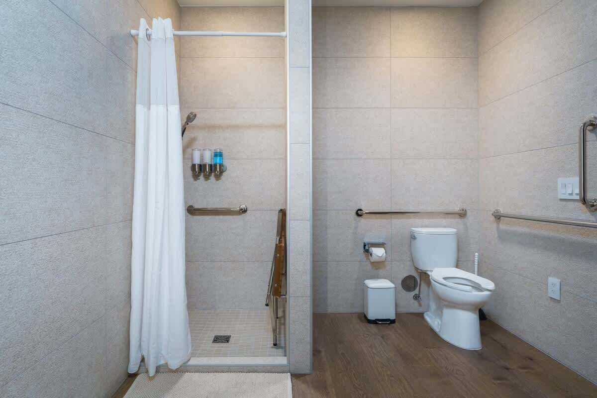 A modern bathroom with a shower, toilet, and grab bars.