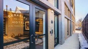 L’entrée d’un hôtel, avec une porte en verre, une façade en briques et un trottoir recouvert de neige.