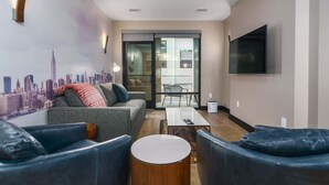 Un salon moderne comprenant un canapé, deux fauteuils, une table basse et un téléviseur fixé au mur.