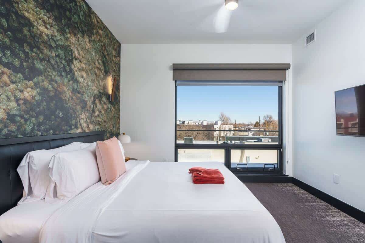 Quarto de hotel com cama grande, vista por uma porta deslizante e televisão na parede.