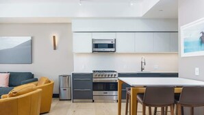 Une cuisine moderne équipée d’un four encastré, d’un micro-ondes et de meubles en acier inoxydable. On y trouve une table à manger avec des chaises, ainsi qu’un canapé dans l’espace salon.