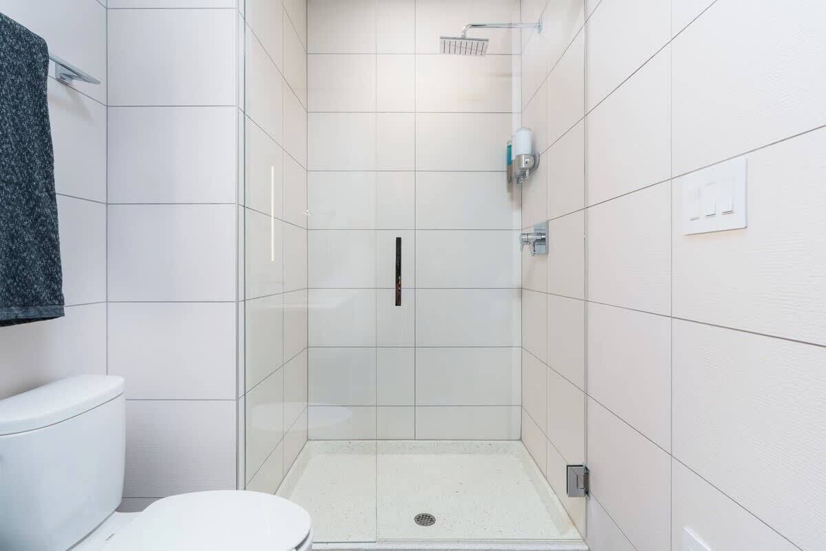 A modern bathroom with white tiles, a shower, and a toilet.
