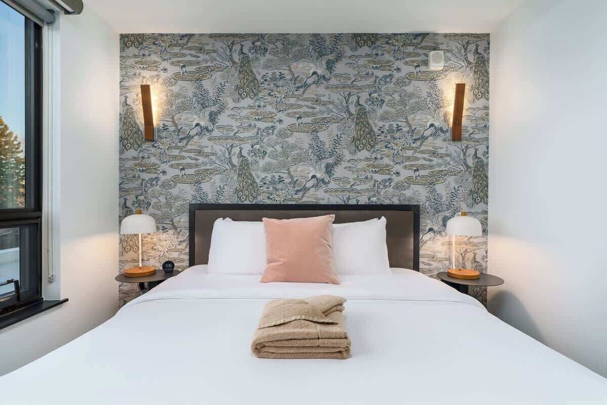A hotel room with a large bed, two bedside tables with lamps, a decorative wall with a nature-themed pattern, and a window with a view.