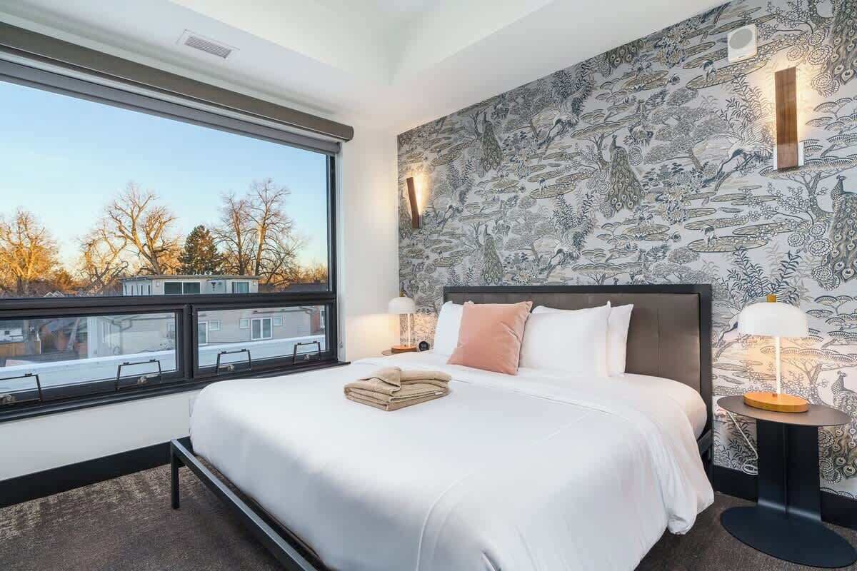 Ein modernes Hotelzimmer mit einem großen Bett, Blick auf die Stadt und einer Wand mit Muster.