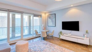 A modern living room with a large window, a flat-screen TV, a round dining table, and a minimalist white console.