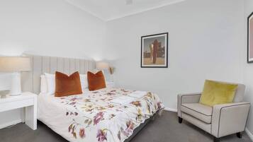 A bedroom with a bed, nightstand, chair, and a framed picture on the wall.