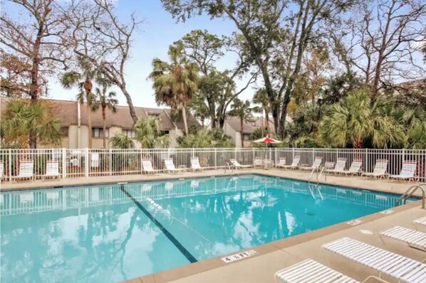 A swimming pool with white lounge chairs and a white fence.