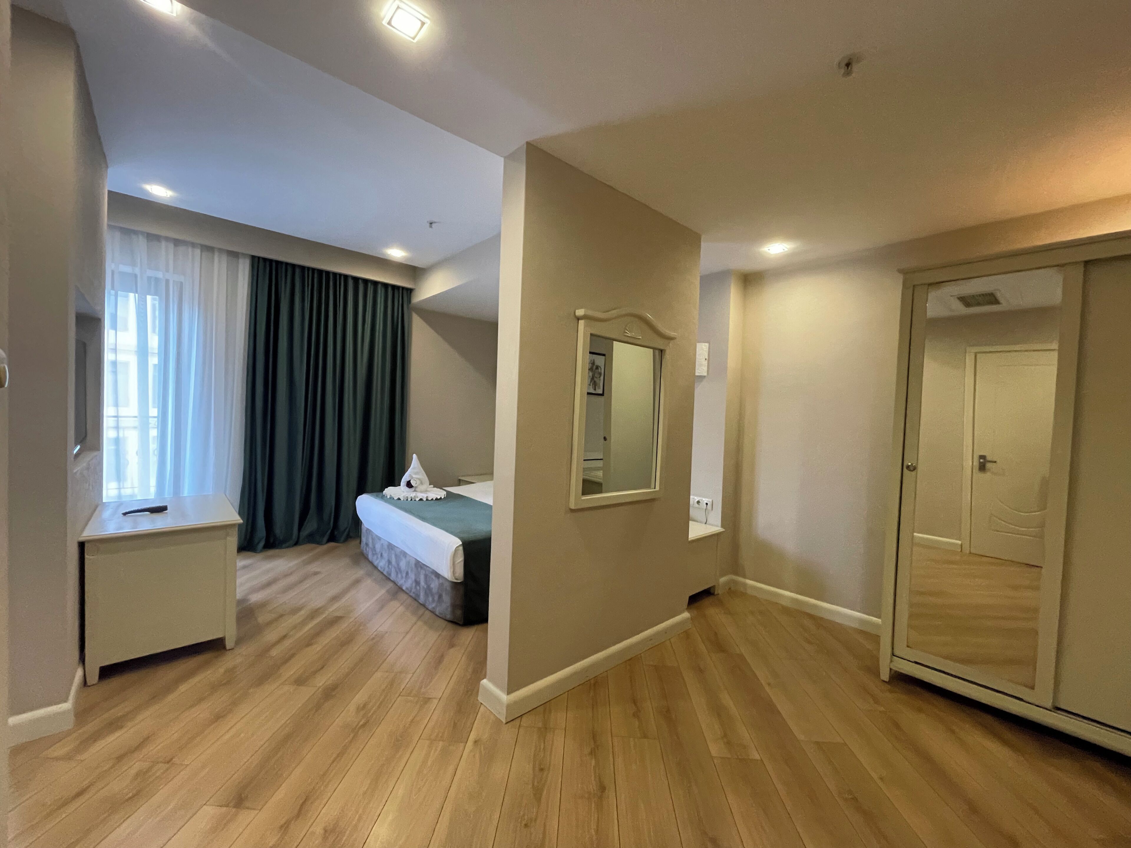 A hotel room with a bed, a desk, a mirror, a wardrobe, and a window with curtains.